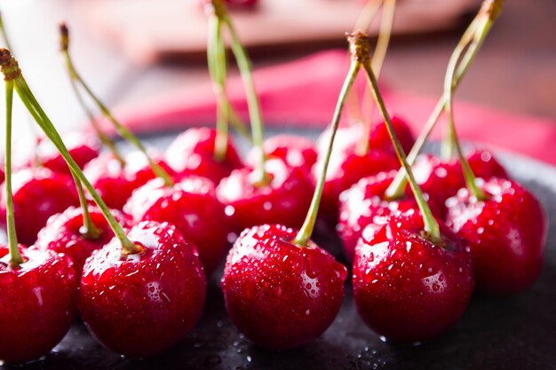 Cerezas en un plato negro Cerezas dulces en una tabla de madera Bayas rojas en gotas de agua en una servilleta roja