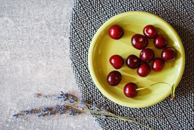 Cerezas en un plato verde sobre una mesa de mármol gris