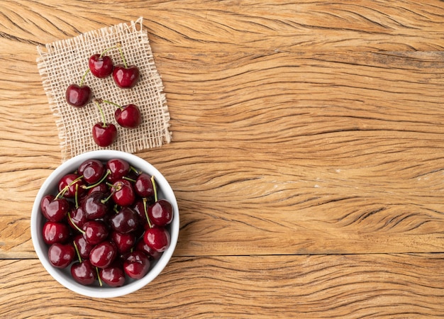 Cerezas rojas en un bol sobre una mesa de madera con espacio para copiar