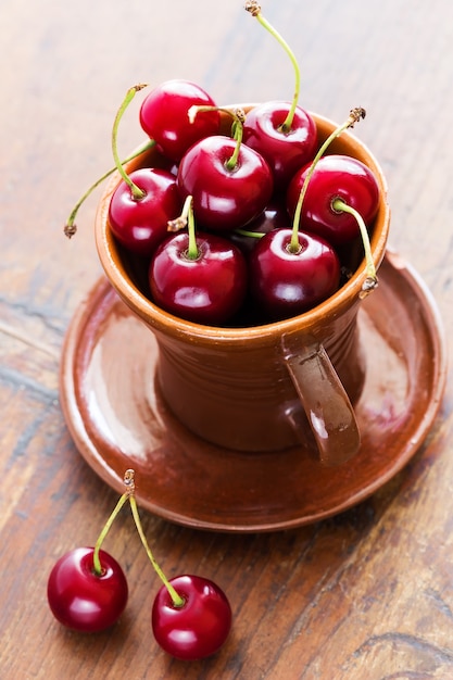 Cerezas rojas frescas en un recipiente sobre una mesa de madera