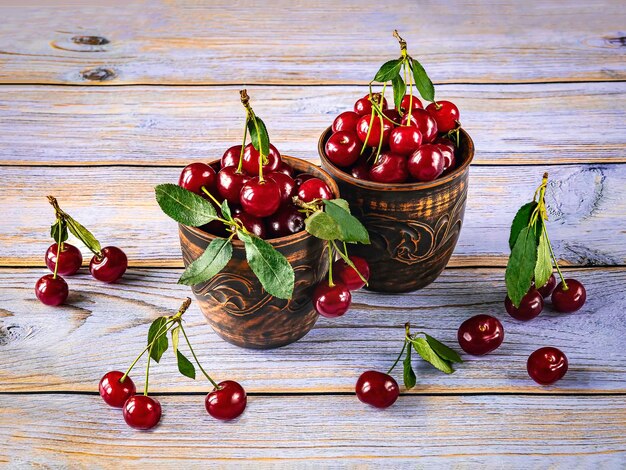 Cerezas rojas maduras en dos tazas de arcilla marrón vintage sobre un fondo de madera Vista superior de la cosecha de verano