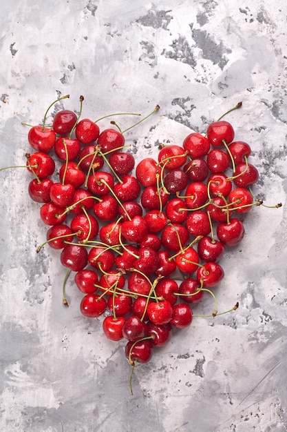 Cerezas rojas maduras sobre fondo gris dispuestas en forma de corazón