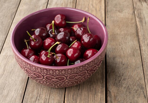 Cerezas rojas en un recipiente sobre una mesa de madera.