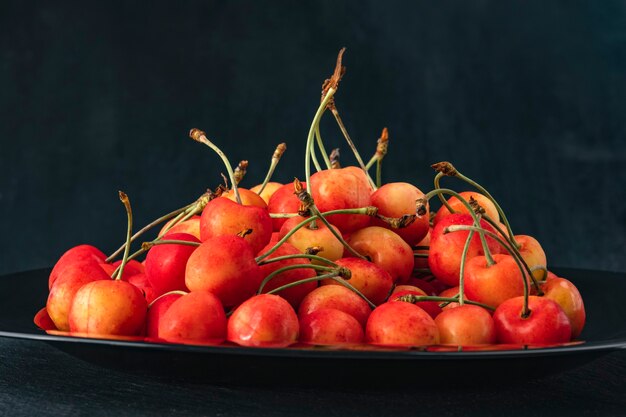 Cerezas rosadas en un plato sobre fondo negro vista lateral. Cerezas maduras y jugosas. Bayas de temporada. De cerca