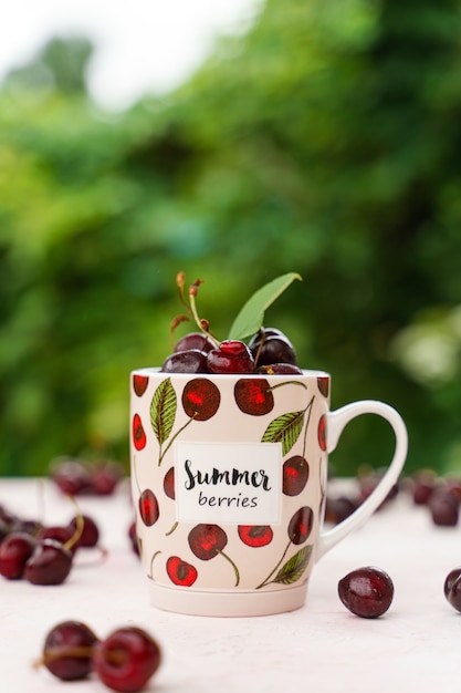 Cerezas en una taza de té en la mesa de jardín contra el follaje verde