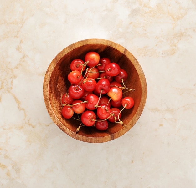 Cerezas en un tazón de madera sobre mármol