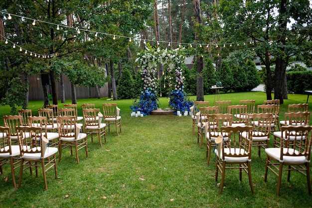 Cerimônia de casamento ao ar livre em um gramado verde. Arco para uma cerimônia de casamento de flores frescas em branco e azul e cadeiras em ouro para convidados. Foco seletivo suave.