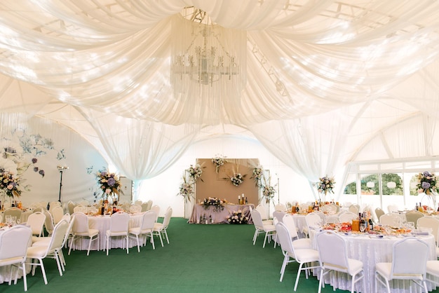 Cerimônia de casamento em uma bela tenda Salão com mesas de jantar decoradas com buquês de flores