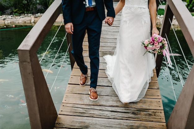 Cerimônia de casamento perto do lago vista do casal de noivos recém-casados caminhando ao longo da ponte sobre um lago ou rio