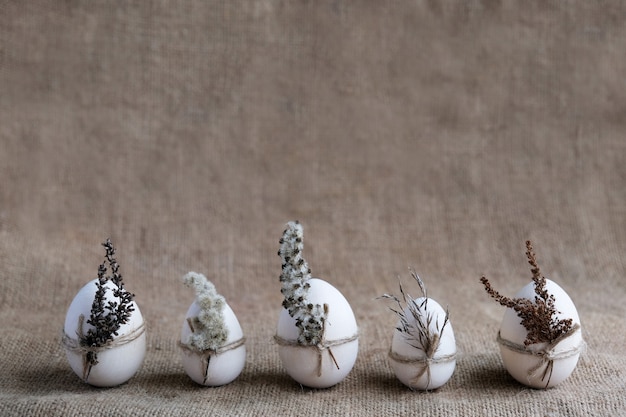 Foto cero desperdicio, vegano, concepto de pascua sostenible. fila de huevos decorados con flores secas sobre fondo de arpillera natural. sensación de naturaleza, postal ecológica. imagen floral cambiante color tierra beige.