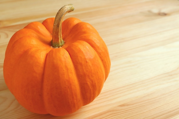 Cerrado de color naranja vivo calabaza madura con tallo en la mesa de madera de color marrón claro.