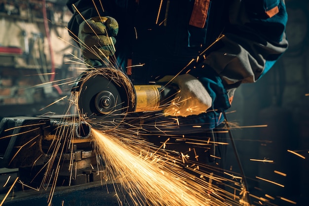 Foto cerrajero en ropa especial y gafas trabaja en producción. procesamiento de metales con amoladora angular