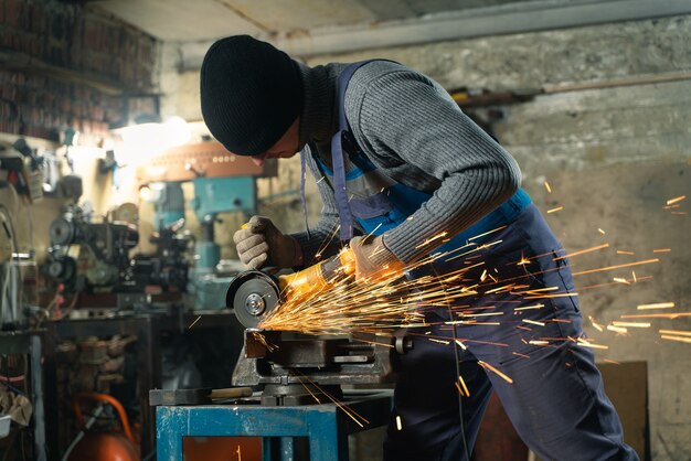 Cerrajero en ropa especial y gafas trabaja en la producción de procesamiento de metales con amoladora angular