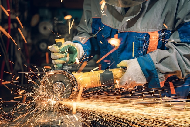 Cerrajero en ropa especial y gafas trabaja en la producción de procesamiento de metales con amoladora angular