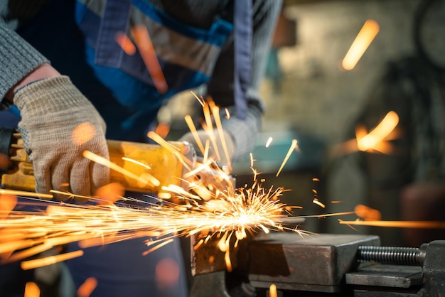 Cerrajero en ropa especial y gafas trabaja en la producción de procesamiento de metales con amoladora angular