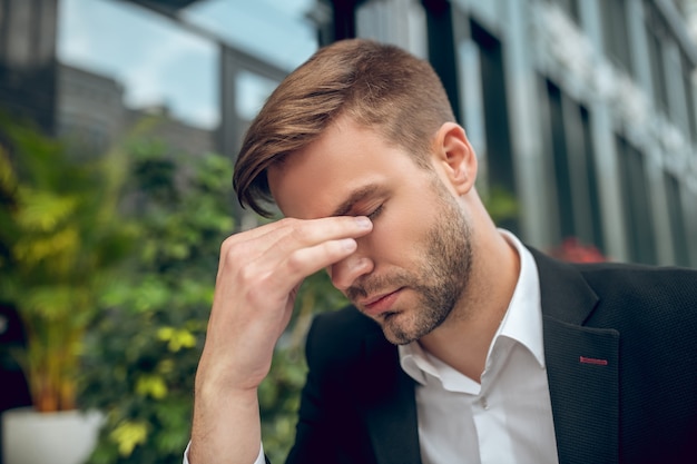 Cerrar apuesto joven empresario en traje negro con aspecto cansado