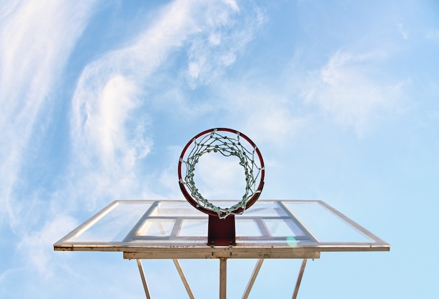 Cerrar el aro de baloncesto vacío en la cancha al aire libre sobre un fondo de cielo azul, vista de ángulo bajo, directamente debajo