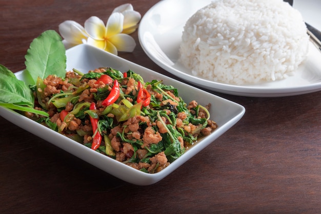 Cerrar arroz con carne de cerdo frita con hojas de albahaca en un plato blanco sobre la mesa de color marrón oscuro