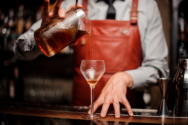 Cerrar barman vertiendo cóctel de alcohol rojo brillante en vidrio elegante