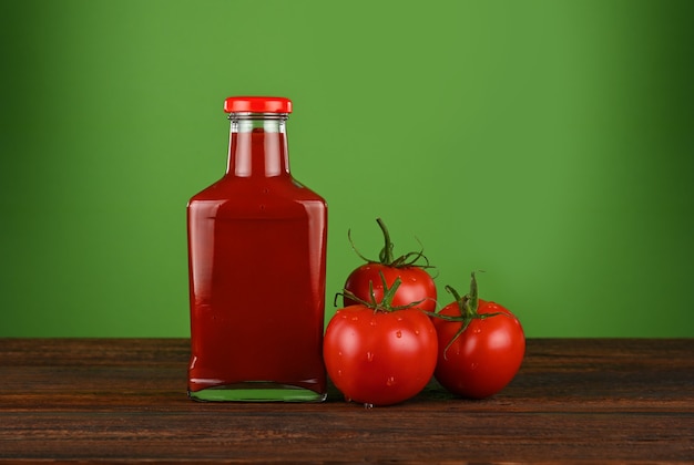 Cerrar una botella de vidrio de salsa de tomate y tomates rojos frescos en la mesa de madera sobre fondo verde con espacio de copia, vista de ángulo bajo