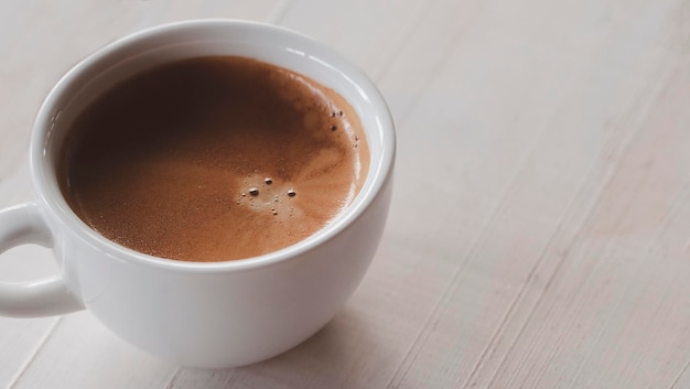 Cerrar café expreso caliente en taza blanca sobre mesa de madera blanca