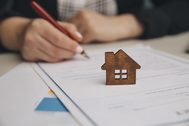 Cerrar la casa de juguete de madera con la mujer firma un contrato de compra o hipoteca para una casa