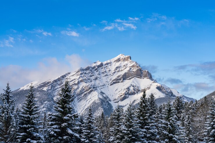 Cerrar Cascade Mountain cubierto de nieve con bosque nevado sobre el cielo azul y las nubes blancas en invierno
