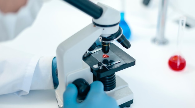 Cerrar científico mirando una gota de sangre a través de un microscopio