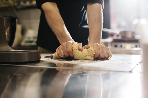 Cerrar El cocinero amasa la masa con las manos haciendo macarrones o pasteles