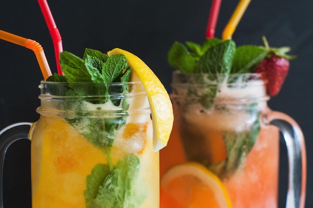 Cerrar cócteles frescos en frasco de vidrio sobre fondo negro para satisfacer la sed Bebida fría de naranja y fresa con refresco de menta y hielo cuando hace calor