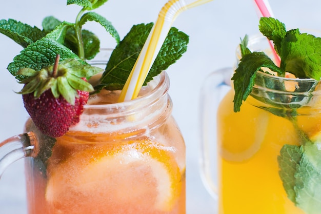 Cerrar cócteles de frutas frescas en frasco de vidrio sobre fondo azul claro Bebida fría de naranja y fresa con refresco de menta y hielo cuando hace calor