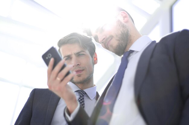 Cerrar compañeros de trabajo mirando la pantalla del teléfono inteligentepersonas y tecnología