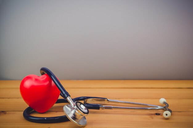 Cerrar corazón rojo y un steythoscope en mesa de madera vieja