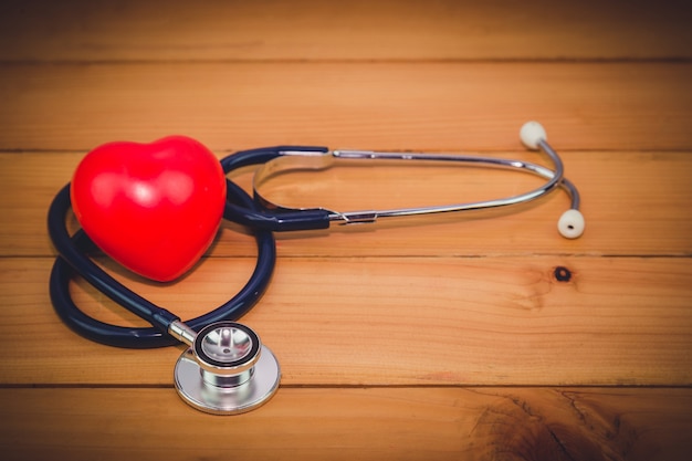 Cerrar corazón rojo y un steythoscope en mesa de madera vieja