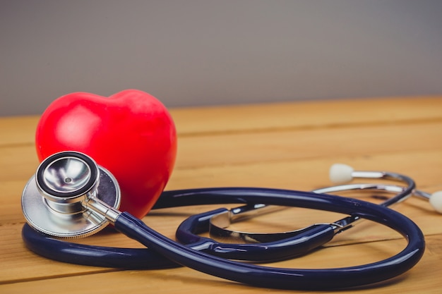 Cerrar corazón rojo y un steythoscope en mesa de madera vieja