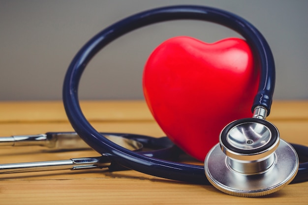 Cerrar corazón rojo y un steythoscope en mesa de madera vieja