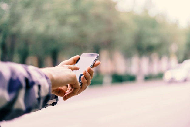 Cerrar los dedos de las manos tocando el teléfono inteligente en la ciudad