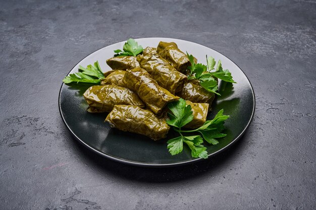 Cerrar deliciosas hojas de parra rellenas dolma con perejil en placa negra sobre fondo de madera oscura.