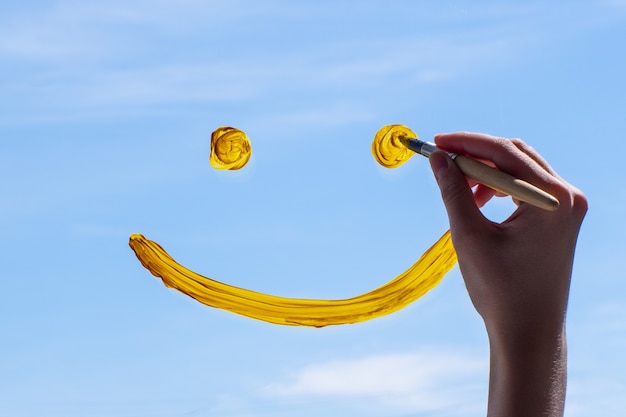 Foto cerrar dibujo a mano alzada una cara sonriente en el cristal contra un cielo azul