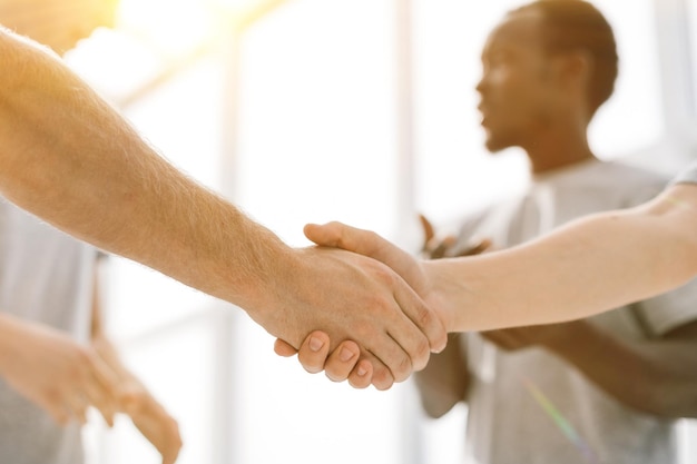 Cerrar dos camaradas dándose la mano de pie en un círculo de amigos