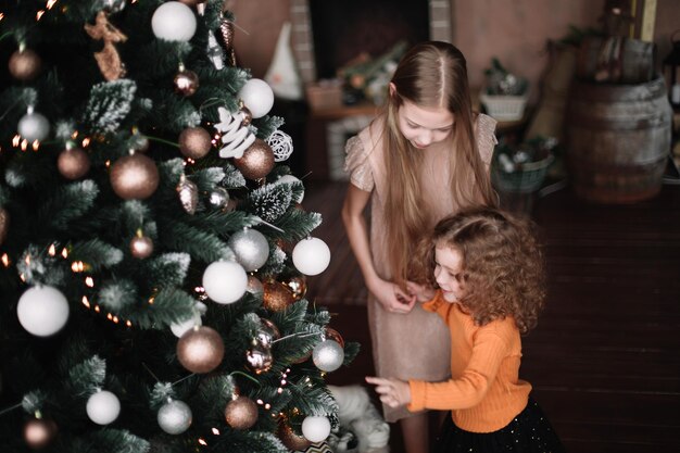 Cerrar dos hermanas de pie junto al árbol de navidad