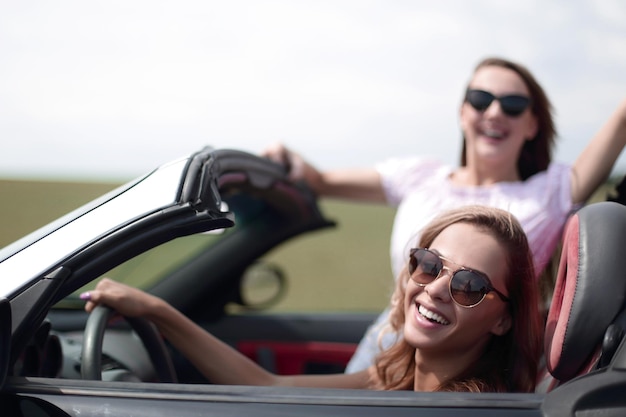 Cerrar dos mujeres jóvenes felices en un coche convertible estilo de vida de moda