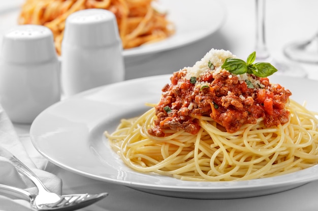 Cerrar espaguetis a la boloñesa italianos cubiertos con queso y albahaca en un plato blanco liso