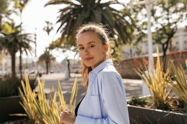 Foto cerrar la foto al aire libre de una chica bonita romántica con camisa azul posando en la cámara y disfrutando de caminar en el verano la chica sonriente se relaja al aire libre bebiendo café