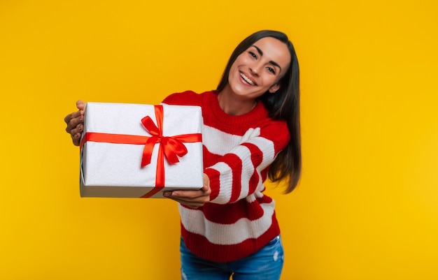 Cerrar foto de atractiva mujer morena joven emocionada feliz sonriente con caja de regalo en manos aisladas sobre fondo amarillo