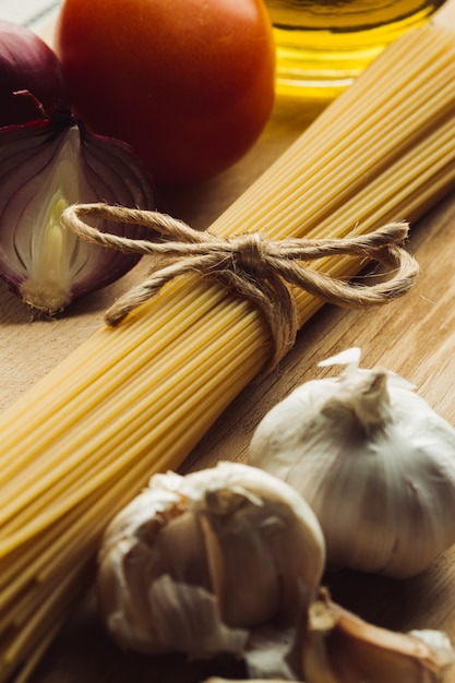 Cerrar foto de bulbos de cebolla, tomate y ajo que rodean el manojo de espaguetis con un lazo de cuerda en él
