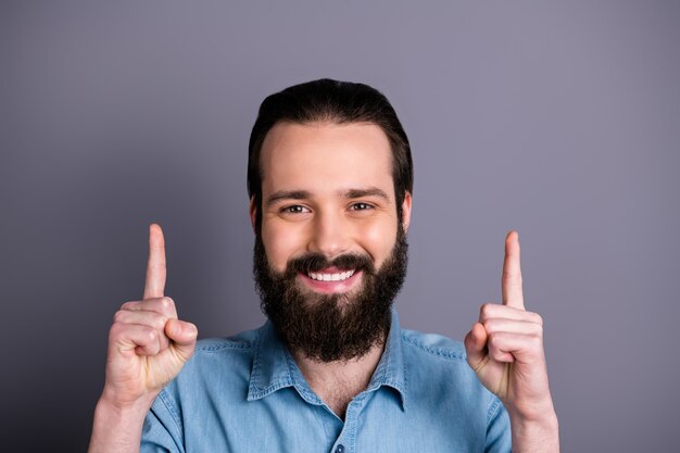 Cerrar foto de chico positivo señalar con el dedo índice hacia arriba espacio de copia demostrar anuncios promo recoger consejos ropa de estilo casual de guerra aislada sobre pared de color gris