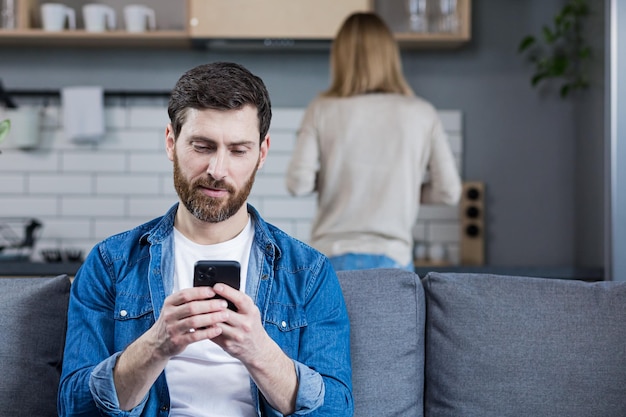 Cerrar foto Conflicto pareja joven familia hombre y mujer El hombre se sienta en el sofá mira el teléfono juega juegos no presta atención a la mujer evita