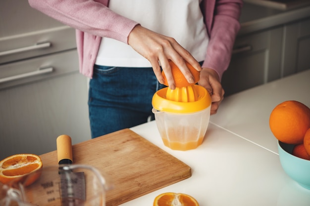 Cerrar foto de una dama caucásica haciendo jugo de naranja sobre la mesa con un exprimidor