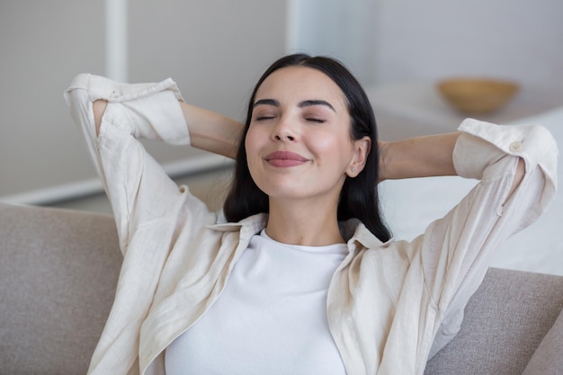 Cerrar foto feliz joven hermosa mujer relajándose en casa en el sofá con los ojos cerrados brazos detrás